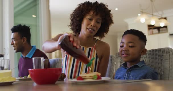 Afroamerikansk Far Ler Medan Han Häller Lönnsirap Pannkakor Till Sonen — Stockvideo