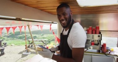 Yemek kamyonunda sosisli hazırlarken gülümseyen Afro-Amerikan bir adamın portresi. yemek kamyonu ve sokak yemekleri konsepti