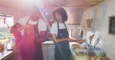 Afro-Amerikalı çift önlük giyip dijital tablet kullanıyor ve yemek kamyonunda sosisli hazırlıyorlar. yemek kamyonu ve sokak yemekleri konsepti