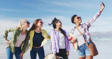 Bir grup mutlu bayan arkadaş sahilde akıllı telefonla selfie çekiyorlar. Tatil, özgürlük ve boş zaman.