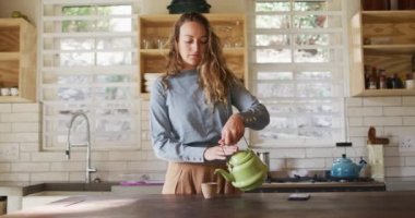 Kır evinde tezgahta duran mutlu beyaz kadın çaydanlıktan çay doldurup gülümsüyor. Kırsal kesimlerin dışında basit bir evde yaşamak.