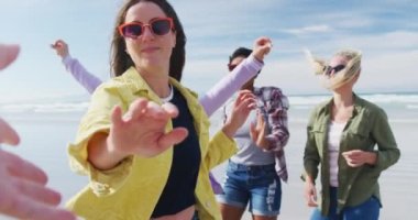 Mutlu bir grup kadın arkadaş sahilde eğleniyor, dans ediyor ve gülümsüyor. Tatil, özgürlük ve boş zaman.