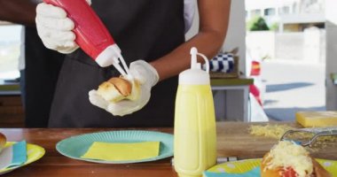 Afro-Amerikan kadının önlük giyip sosisli sandviçe ketçap koyduğu orta bölüm. yemek kamyonu ve sokak yemekleri konsepti