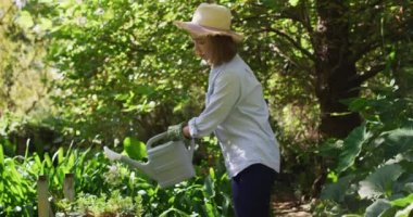 Güneşli bir günde Asyalı kadın bahçıvanlık yapıyor ve gülümsüyor. Karantina süresince evde tecrit altında..