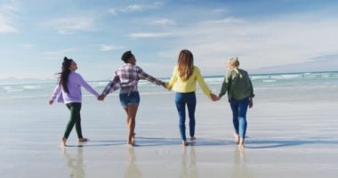 Mutlu bir grup kadın arkadaş sahilde el ele yürüyüp eğleniyorlar. Tatil, özgürlük ve boş zaman.