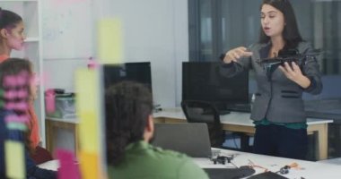 Beyaz bir kadın İHA 'yı elinde tutarak çeşitli meslektaşlarına sunum yapıyor. Bağımsız yaratıcı bir şirkette çalışmak..