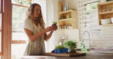 Gülümseyen beyaz kadın, güneşli kır evinde duran saksı bitkileriyle ilgileniyor. Sağlıklı yaşam, kırsal kesimde doğaya yakın yaşam..