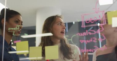 Cam duvarın yanında duran çeşitli kadın iş arkadaşları beyin fırtınası yapıyorlar. Bağımsız yaratıcı bir şirkette çalışmak.