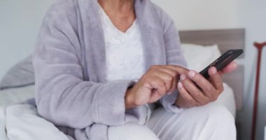 Afro-Amerikan son sınıf öğrencisi kadının evde yatakta otururken akıllı telefon kullandığı bölüm. emeklilik yaşlılar için karantina konsepti