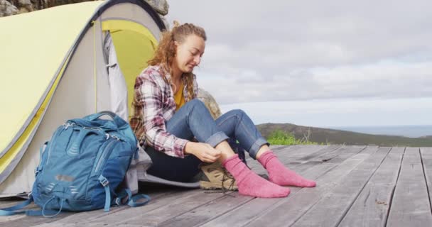 幸せな白人女性のキャンプは テントの外に座って農村部の山の中腹に設定でブーツを着る 健康的な生活 オフグリッド 自然に近い — ストック動画
