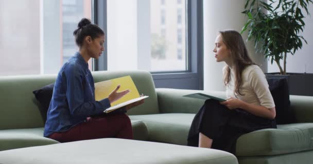 Dos Diversas Compañeras Trabajo Sentadas Sofá Sosteniendo Documentos Hablando Trabajar — Vídeos de Stock