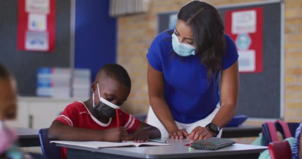 Zróżnicowana Nauczycielka Pomaga Uczniowi Lekcjami Wszyscy Noszą Maski Twarzy Dzieci — Wideo stockowe