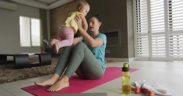 自宅でヨガマットでヨガを練習しながら 赤ちゃんと遊ぶ白人の母親 母の日愛の親子の子供時代のコンセプト — ストック動画