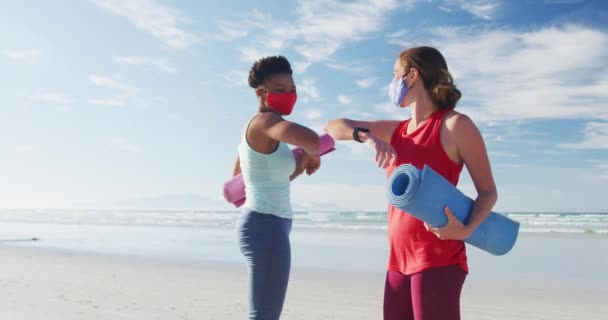 Forskellige Kvindelige Venner Iført Ansigtsmasker Holder Yogamåtter Stranden Rører Albuer – Stock-video