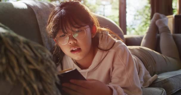 Menina Asiática Sorrindo Enquanto Livro Enquanto Está Sentado Sofá Casa — Vídeo de Stock