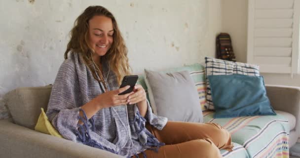 Glimlachende Blanke Vrouw Met Deken Zittend Bank Met Smartphone Huiskamer — Stockvideo