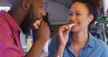 Afro-Amerikan çiftlerin yemek kamyonunda hamburger ve patates kızartması yediği yakın çekim. yemek kamyonu ve sokak yemekleri konsepti