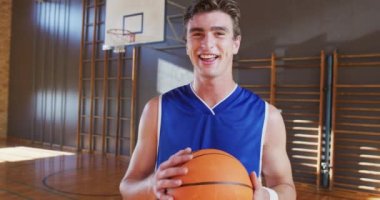 Kafkas erkek basketbolcunun top tutarken ve gülümserken portresi. Basketbol, kapalı sahada spor eğitimi..