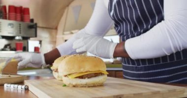 Afrika kökenli Amerikalı adamın önlük giyip ahşap tepsinin üzerine hamburger ve patates kızartması koyduğu bölüm. yemek kamyonu ve sokak yemekleri konsepti