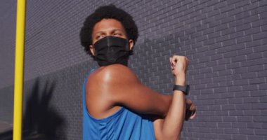 Formda Afro-Amerikan bir adam şehirde yüz maskesi takarak egzersiz yapıyor, sokakta geriniyor. fitness ve aktif şehir dışı yaşam tarzı.
