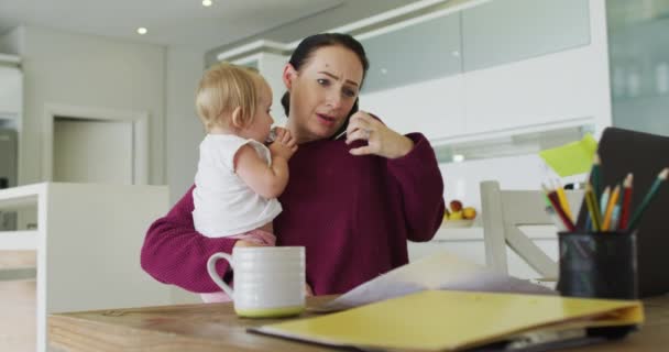 Madre Caucásica Sosteniendo Bebé Hablando Teléfono Inteligente Mientras Trabaja Desde — Vídeos de Stock