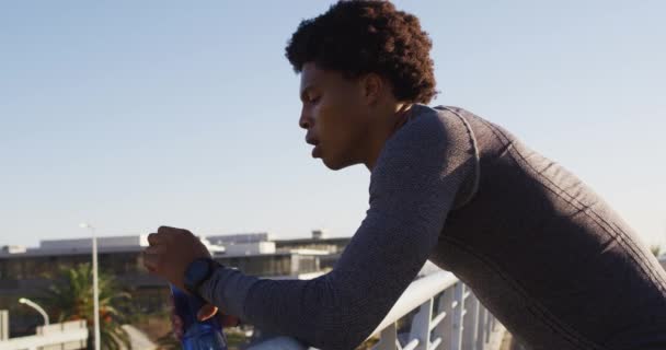 アフリカ系アメリカ人の男性が街で運動し 歩道橋の上で休み 水のボトルから飲むのに適しています フィットネスとアクティブな都会のアウトドアライフスタイル — ストック動画