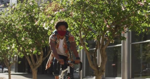 街のアフリカ系アメリカ人の男は 顔マスク自転車に乗って路上で身に着けている 市内ではコロナウイルスが19種のパンデミックを起こし — ストック動画