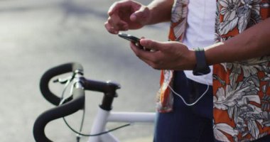 Sokakta bisikleti akıllı telefon kullanan Afro-Amerikan bir adamın orta kesimi. Dijital göçebe şehirde geziyor, dolaşıyor..