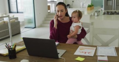 Beyaz bir anne bebeğini kucağında tutuyor ve evde çalışırken telefonla konuşuyor. annelik, sevgi ve çocuk bakımı kavramı