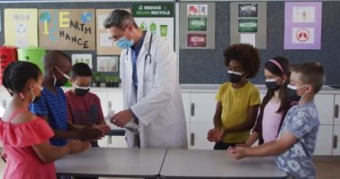 Çeşitli okul öğretmenleri ve okul çocukları ellerini dezenfekte ediyor, hepsi maske takıyor. Coronavirus covid 19 salgını sırasında ilkokuldaki çocuklar