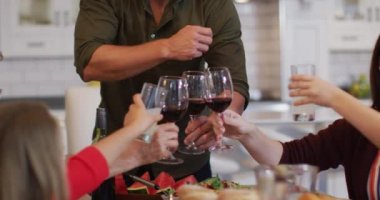 Gülümseyen beyaz anne yemekten önce sofrada çok nesilli bir aileyle kadeh kaldırıyor. çok nesildir birlikte evde vakit geçiriyoruz..