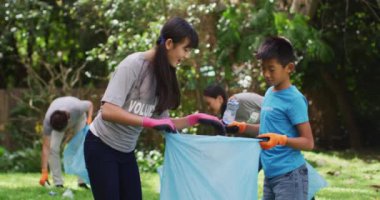 Gülümseyen Asyalı kardeşler çöp torbası tutuyor, plastik atık topluyor ve beşlik çakıyorlar. Çevre koruma gönüllüleri kırsal alanda temizlik yapıyor..