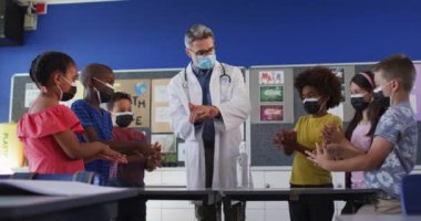 Çeşitli okul öğretmenleri ve okul çocukları ellerini dezenfekte ediyor, hepsi maske takıyor. Coronavirus covid 19 salgını sırasında ilkokuldaki çocuklar