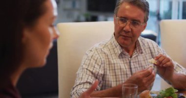 Gülümseyen beyaz büyükbaba aile yemeği sırasında geliniyle konuşuyor ve masada yemek yiyor. çok nesildir birlikte evde vakit geçiriyoruz..