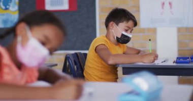 Ders sırasında sınıfta oturan beyaz bir çocuğun portresi, yüz maskesi takarak notlar alıyor. Coronavirus covid 19 salgını sırasında ilkokuldaki çocuklar.