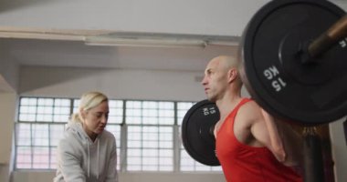 Beyaz kaslı adam kadın antrenörle ağırlık kaldırıyor. Spor salonunda sağlık ve spor eğitimi.