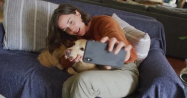 Gülümseyen beyaz kadın akıllı telefonuyla selfie çekiyor ve evcil köpeğini okşuyor. Yaşam tarzı, evcil hayvan, arkadaşlık ve hayvansal arkadaşlık kavramı.