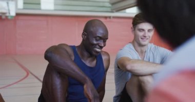 Çeşitli erkek basketbol takımı ve antrenör maçtan sonra dinleniyor ve konuşuyor. Basketbol, kapalı sahada spor eğitimi..