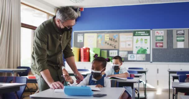 Разнообразный Учитель Мужчина Помогающий Школьнице Сидеть Классе Масках Лица Дети — стоковое видео