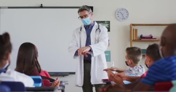 Mångsidig Lärare Desinficerar Händerna Klassrummet Med Skolbarn Sittande Ansiktsmasker Barn — Stockvideo