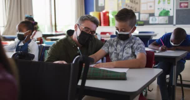 Mångsidig Manlig Lärare Hjälpa Skolpojke Sitter Klassrummet Alla Bär Ansiktsmasker — Stockvideo