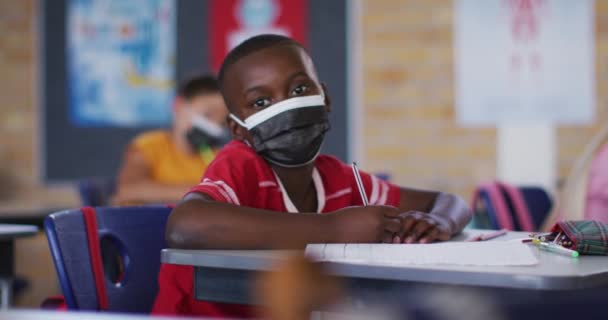 Portræt Afrikansk Amerikansk Skoledreng Iført Ansigtsmaske Sidder Klasseværelset Kigger Kameraet – Stock-video