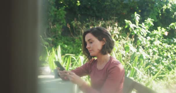 Mulher Branca Sorridente Usando Smartphone Sentado Mesa Jardim Ensolarado Conceito — Vídeo de Stock