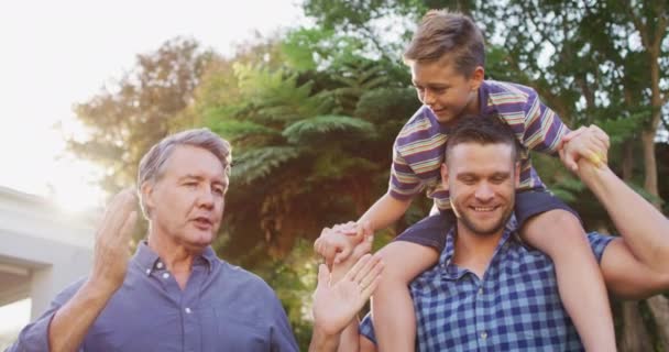 快乐的高加索祖父与孙子说话 坐在父亲的肩上花园 快乐的家庭在家里共度时光 — 图库视频影像