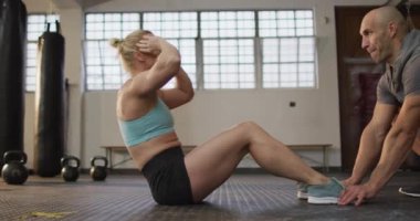 Spor salonunda erkek antrenör bacaklarını tutarken beyaz bir kadın mekik çekiyor. Spor, antrenman ve spor konsepti