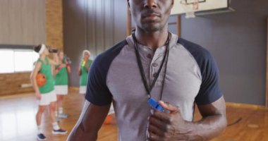 Arka planda çeşitli bayan basketbol takımları olan Afrika kökenli Amerikalı erkek koçun portresi. Basketbol, kapalı sahada spor eğitimi..