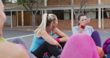 Çeşitli bayan basketbol takımları sahada oturup konuşuyorlar. Basketbol, şehir merkezinde spor eğitimi..