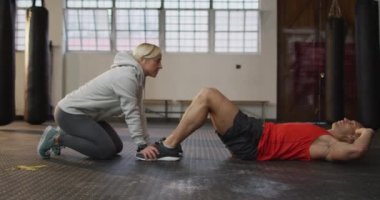 Beyaz kaslı adam egzersiz yapıyor, kadın koçla mekik çekiyor. Spor salonunda sağlık ve spor eğitimi.