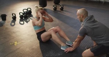 Spor salonunda erkek antrenör bacaklarını tutarken beyaz bir kadın mekik çekiyor. Spor, antrenman ve spor konsepti