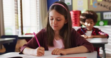 Sınıfta oturan, notlar alan, kameraya bakan beyaz bir kızın portresi. İlkokuldaki çocuklar yazın. a